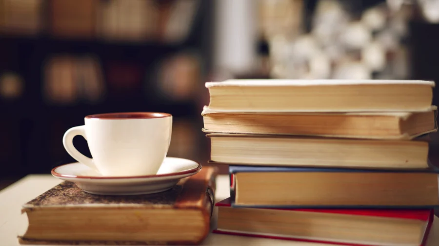 A stack of colorful quote books on a wooden table, surrounded by a cup of coffee and a potted plant